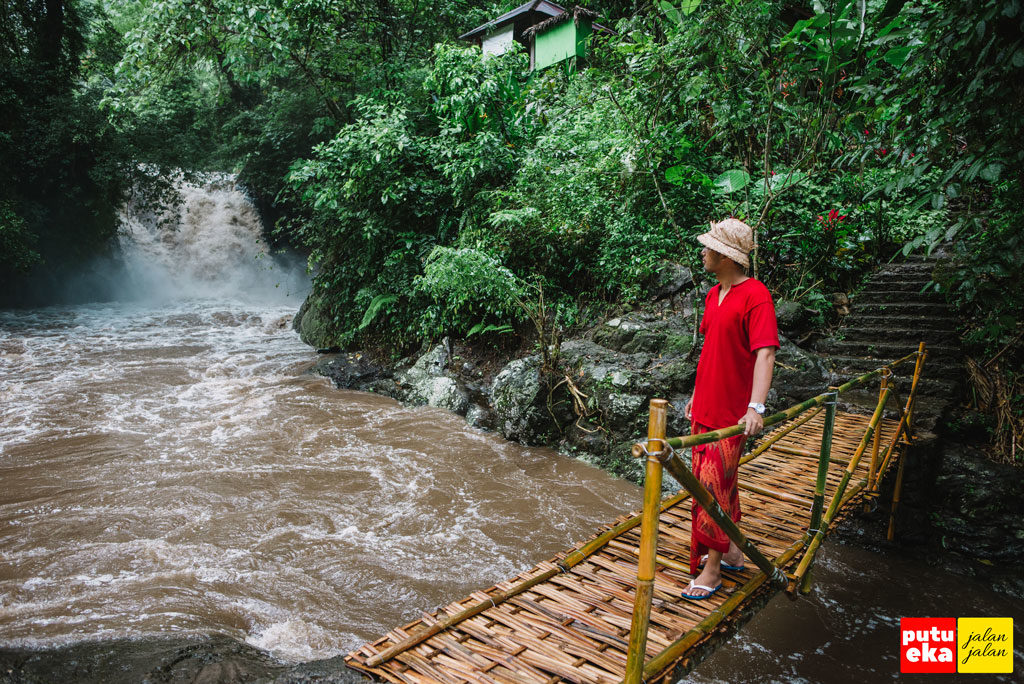 Putu Eka Jalan Jalan sedang berjalan diatas jembatan bambu di bagian hilir air terjun