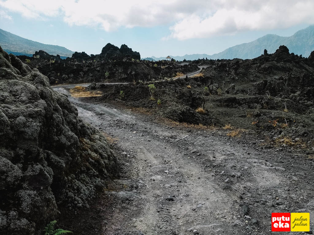 Jalan berdebu meliuk melewati batuan lava yang menghitam